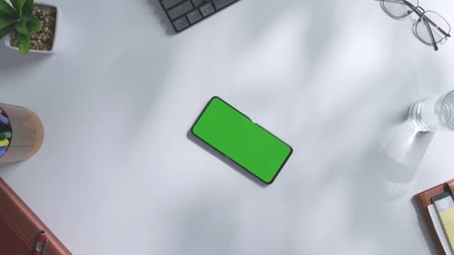 Top down view of mock up green screen smartphone and laptop on a white desk