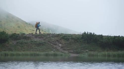 A tourist with a backpack goes on a hike along a mountain range near a lake