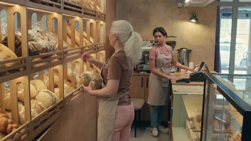 Senior Worker Helping Colleague at Cash Register in Bakery
