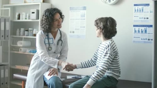 Female Pediatrician Shaking Hands and Speaking with Young Patient in Clinic