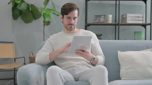 Man Cheering While Using a Tablet Indoors