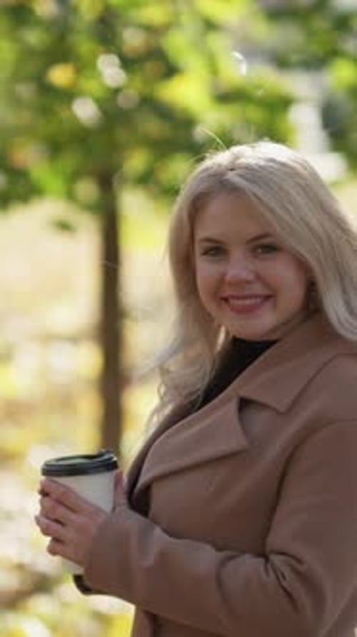 Blonde Woman Smiling in Autumn Park with Coffee
