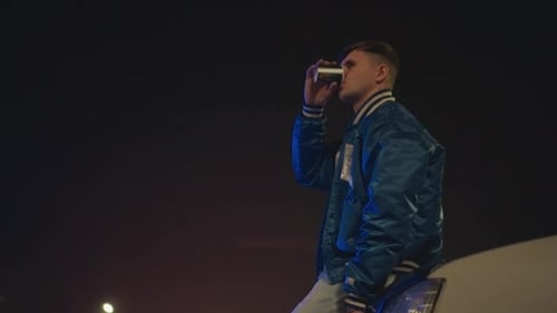 Young Man Drinks Coffee at Night on Car Hood