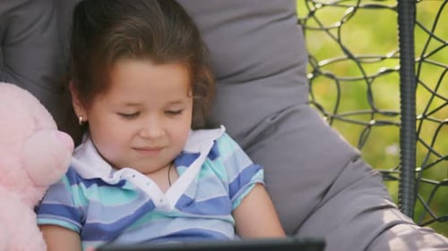 Girl Sits in a Rocking Chair Cocoon with Looks at the Tablet