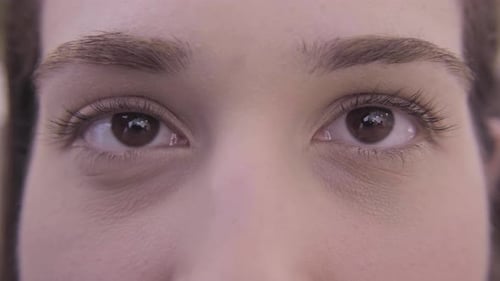 Extreme close up of brown eyes. Young woman winking twice with her right eye. White emotional girl s