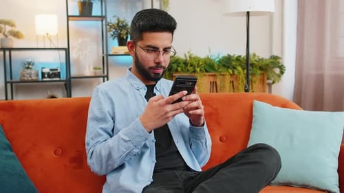 Young Man Using Mobile Phone on Orange Couch