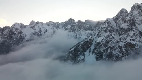Flight above rolling cotton clouds with Alps mountains snowy white peaks. Tilt down aerial cloudscap