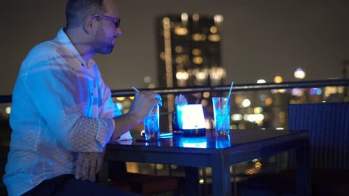Young, Happy Man Drinking Cocktail Sitting on Terrace in Bar at Night Alcohol