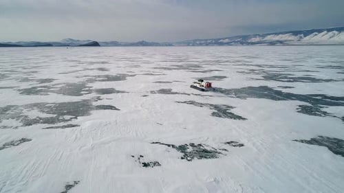 Aerial View on the Hovercraft Driving on Cracked Snowy Ice of Baikal Drone Follows the Vehicle