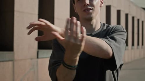 Young man stretching arm muscles outdoors in urban setting