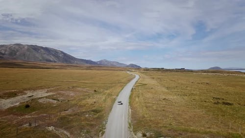 Off-road vehicle on remote unpaved road in sunny New Zealand. Aerial follow shot