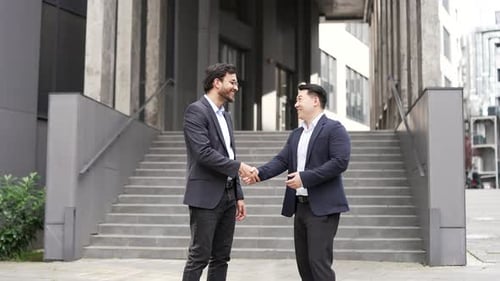 Two businessmen shaking hands outside modern office building, symbolizing successful business