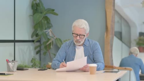 Senior Man Reviews Documents at Office Table