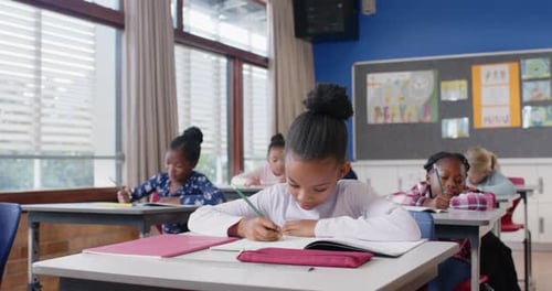 In school, children writing in notebooks at desks, concentrating on assignments