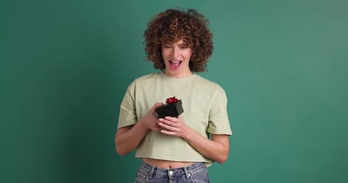 Surprised Woman Opening Gift Box in Green Colored Studio