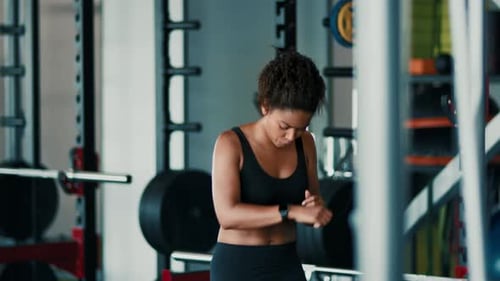 Woman Running on a Treadmill in a Gym With Weights in the Background During Workout Session