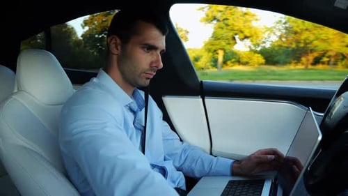 Man Works On Laptop and Phone in Car