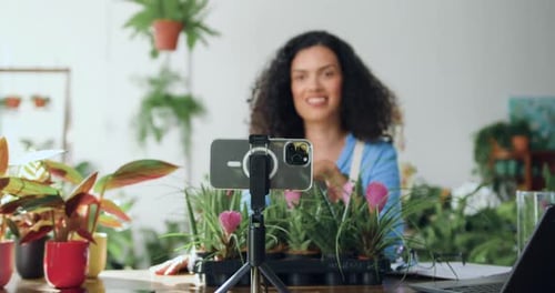 Mujer afroamericana florista en delantal grabando un vídeo en una floristería con el teléfono. Bloguero jardinero
