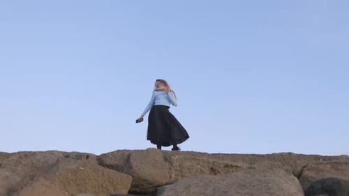 A Woman is Standing on a Rock with Her Arms Raised in the Air