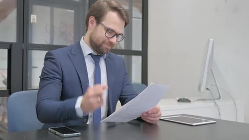 Adult Businessman Reviews Documents at Desk in Office