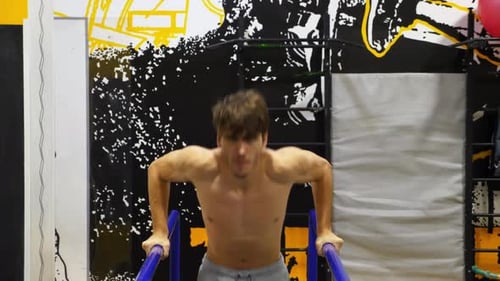 Starker sportlicher Mann macht Liegestütze an Parallelstangen im modernen Fitnessstudio Junger Sportler trainiert in