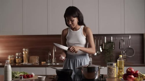 Woman Cracking Egg with Knife in Kitchen