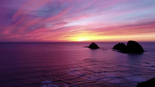 Drone flies over ocean towards sea stacks and beautiful sunset