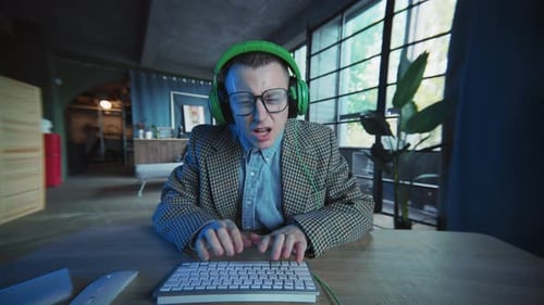 Man Typing on Keyboard Wearing Headphones and Glasses