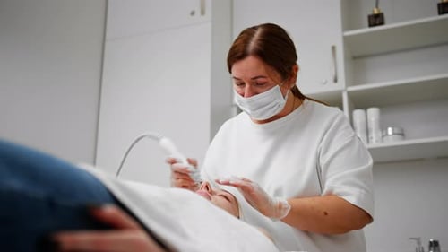 Beautician in gloves conducts vacuum cleaning and polishing face skin of young woman in cosmetology