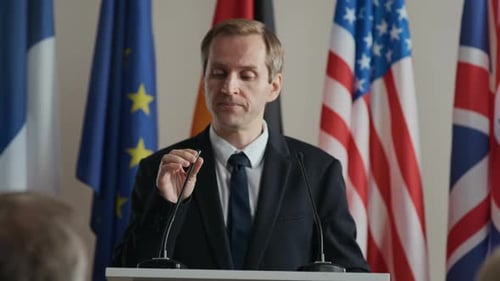 Man Speaking at a Press Conference with Flags