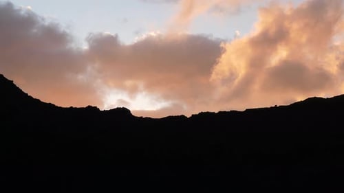 Orange clouds during sunset with mountain silhouette.