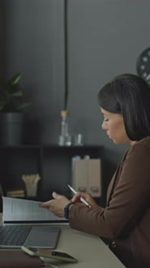 Young Businesswoman Doing Paperwork and Using Laptop in Office