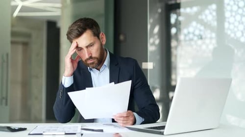 Worried Businessman Reviews Documents in Office