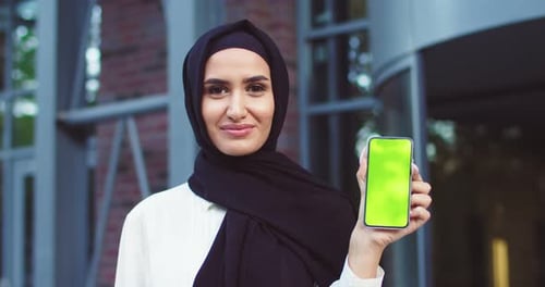 Close Up of Confident Muslim Woman in Black Hijab Holding Smartphone with Greenscreen Modern