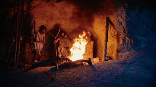 Tribe of Prehistoric Hunter-Gatherers Wearing Animal Skins Stand Around Bonfire Outside of Cave at