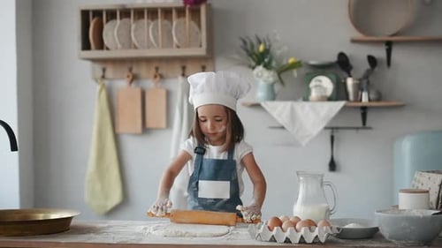 Cute kid in white chef uniform kneading the dough by wooden tool on the kitchen