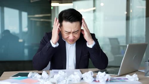 Exhausted asian businessman is bored sitting at workplace at desk in business office. Overworked