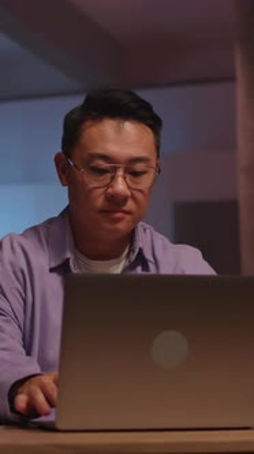 Home Office Scene with Man Focused Person Working Diligently on Laptop in Cozy Nighttime Home Office