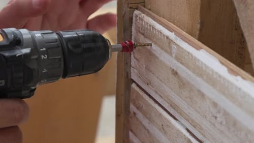 A Man Hands Using a Power Tool Fastens a Board with a Screw Slow Motion