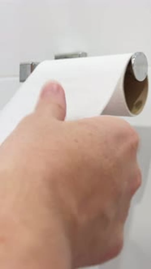 Mans Hands Taking Toilet Paper From a Wall Mounted Toilet Paper Roll