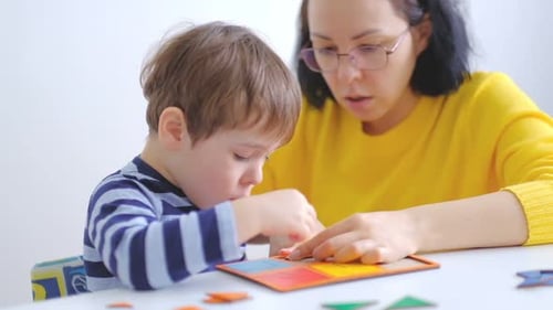 Little Asian Boy Collects Puzzles with Mom Sitting at the Desk A Cute Child Collects a Picture From