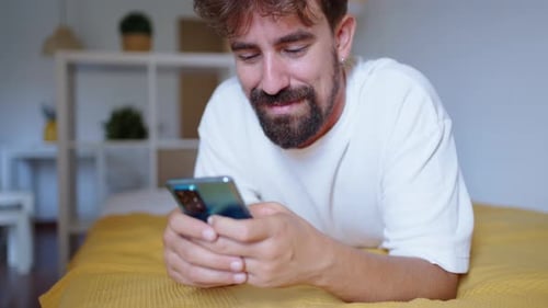 Happy Man Using Smartphone Lying on Bed at Home