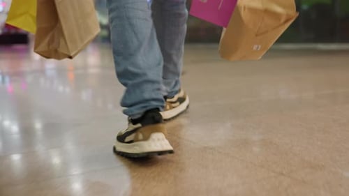 Leg View Of Man Walking With Shopping Bags In Mall