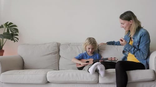 Child Plays Ukulele with Mother on Couch