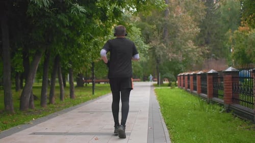 Man Walking Calmly Stroll Past Trees and Fences Solitary Man Enjoying Peaceful City Evening Lone