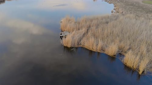 Aerial View of Man Sits on Wooden Bridge Fishing with Fishing Rod in Pond Near Dry Reeds