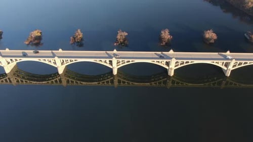 Top down aerial of traffic on bridge. Beautiful reflection of arches in blue river water. Drone shot