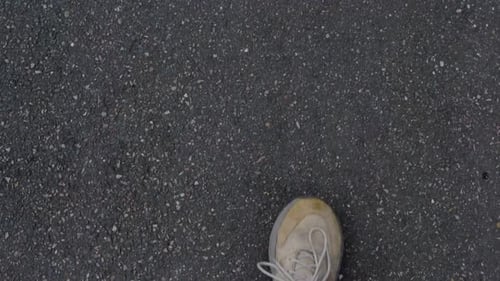 Close-up of dirty sneakers walking over asphalt, showing worn footwear and rough pavement texture