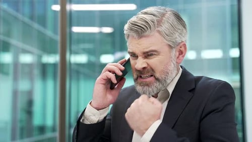 Angry mature businessman arguing talking on mobile phone in office. Excited nervous entrepreneur