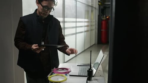Man Using Tablet and Laptop in Server Room